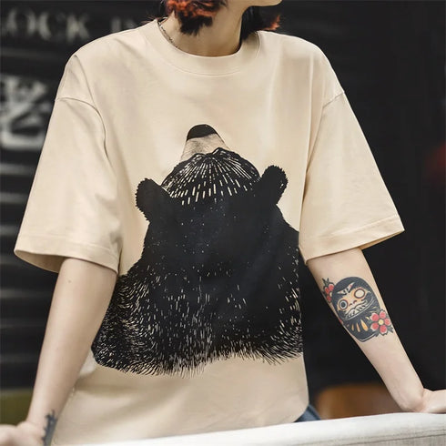 Person wearing a beige t-shirt with a black bear graphic design.